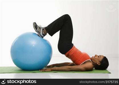 Profile of African American woman stretching on mat with feet on exercise ball.