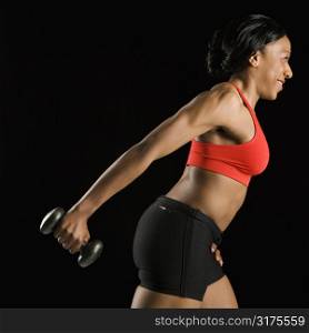 Profile of African American young adult woman holding dumbbell outstretched.