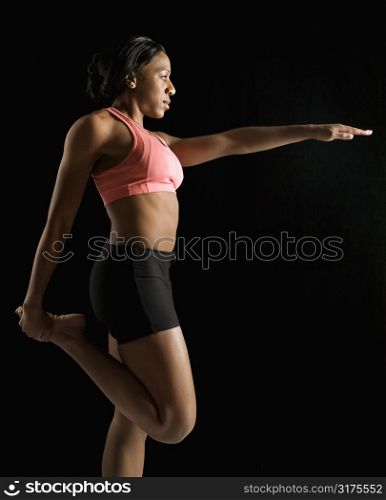 Profile of African American young adult woman stretching leg with arm raised.