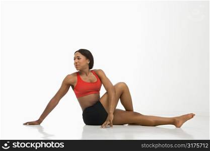 Profile of African American young adult woman stretching on floor.