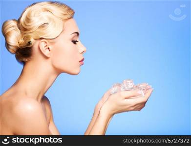 Profile of beautiful young woman with ice in her hands on blue background.