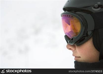 Profile of Caucasian teenage boy skier wearing helmet and goggles at ski resort on mountain.