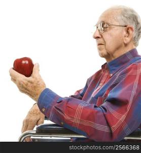 Profile of Caucasion elderly man sitting in wheelchair looking at red apple in his hand.