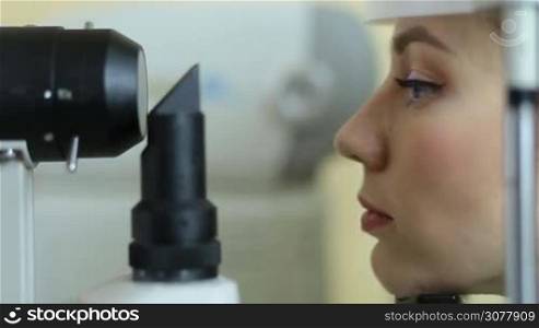 Profile of pretty woman examining eyesight with slit lamp by optometrist at eye clinic. Beautiful female patient checking vision with virtual laser in modern ophthalmology clinic closeup. Eye care concept.