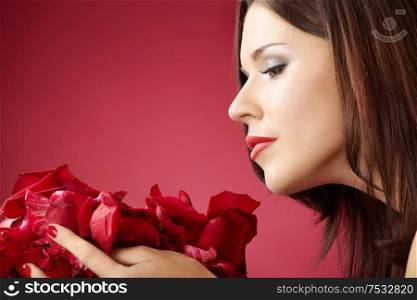 Profile of the girl smelling petals of roses, isolated on a red background