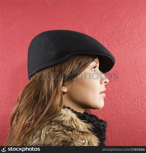 Profile of young brunette adult Caucasian woman wearing flat hat.