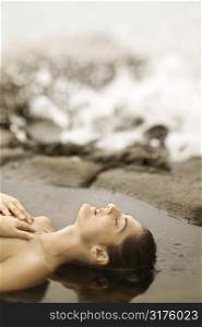 Profile of young nude Caucasian woman lying on beach sunbathing.