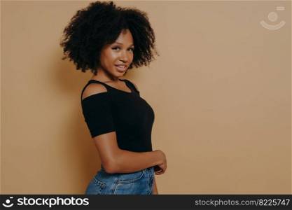 Profile portrait of cute gorgeous african american girl with beaming smile and full lips in casual outfit isolated over dark beige background with copy space for advertising, positive emotions concept. Profile portrait of cute gorgeous african american girl with beaming smile in casual outfit