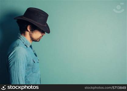 Profile shot of a young cowboy standing against a blue wall