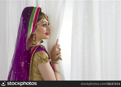 Profile shot of beautiful bride standing by window at home