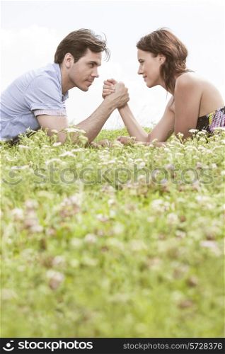 Profile shot of couple arm wrestling while lying on grass against sky
