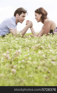 Profile shot of couple arm wrestling while lying on grass against sky