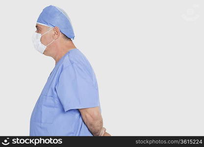 Profile shot of senior male surgeon standing with hands behind back over gray background