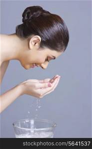 Profile shot of woman washing face with water against blue background
