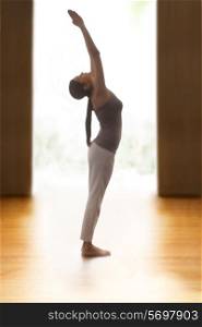 Profile shot of young woman doing back bend yoga pose on hardwood floor