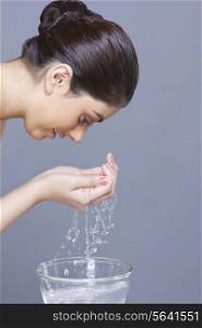 Profile shot of young woman washing face with water over blue background