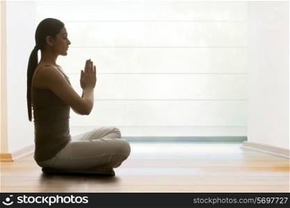 Profile shot of young woman with hands clasped meditating on hardwood floor