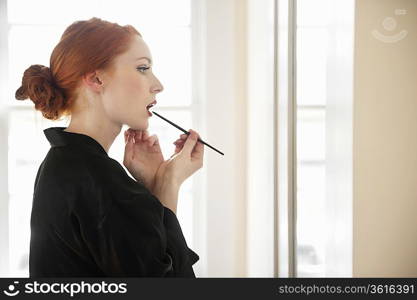 Profile view of a young woman in robe applying lip liner