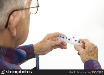 Profile view of Caucasion elderly man holding seven-day pill box with Thursday open.
