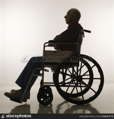 Profile view of silhouetted Caucasion elderly man sitting in wheelchair.