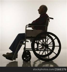 Profile view of silhouetted Caucasion elderly man sitting in wheelchair.