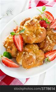 Profiteroles with nuts and strawberries over light background, closeup, selective focus