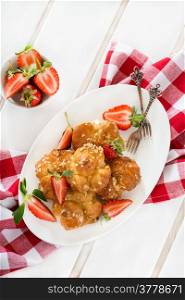 Profiteroles with nuts and strawberries over light background, overhead