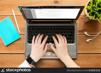 programming, business, people and technology concept - close up of woman or student typing on laptop computer with coding on screen, notebook and earphones on wooden table