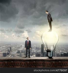 Progress in business. Businessman standing on bulb and looking down at colleague