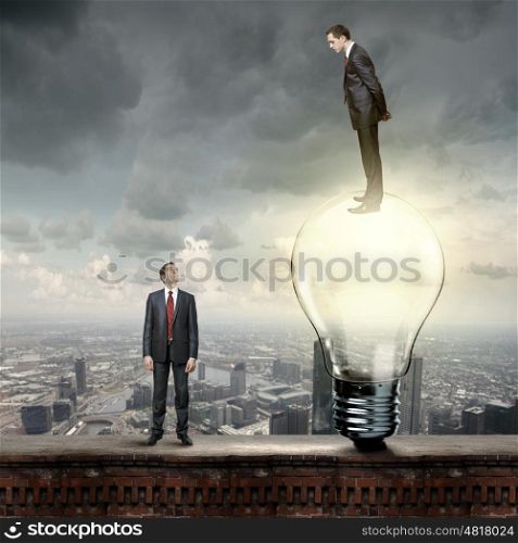 Progress in business. Businessman standing on bulb and looking down at colleague