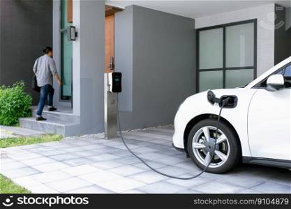 Progressive asian man and electric car with home charging station. Concept of the use of electric vehicles in a progressive lifestyle contributes to a clean and healthy environment.. Progressive concept of asian man and electric car with home charging station.