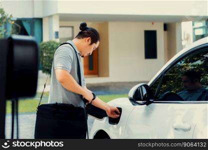 Progressive asian man install cable plug to his electric car with home charging station in the backyard. Concept use of electric vehicles in a progressive lifestyle contributes to clean environment.. Progressive asian man recharge his EV car at home charging station.