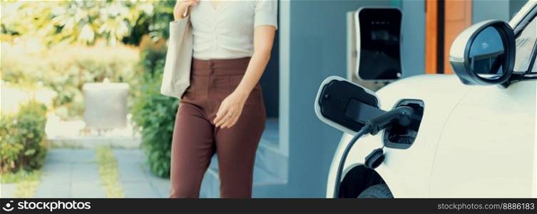 Progressive asian woman and electric car with home charging station. Concept of the use of electric vehicles in a progressive lifestyle contributes to a clean and healthy environment.. Progressive concept of asian woman and electric car with home charging station.