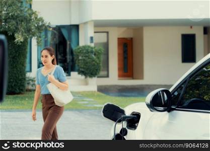 Progressive asian woman and electric car with home charging station. Concept of the use of electric vehicles in a progressive lifestyle contributes to a clean and healthy environment.. Progressive concept of asian woman and electric car with home charging station.