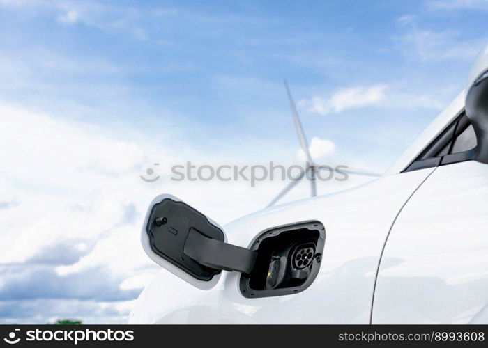 Progressive combination of wind turbine and EV car, future energy infrastructure. Electric vehicle being charged at charging station powered by renewable energy from wind turbine in the countryside.. Progressive combination of EV car, charging station and wind turbine.