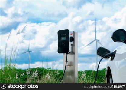 Progressive combination of wind turbine and EV car, future energy infrastructure. Electric vehicle being charged at charging station powered by renewable energy from wind turbine in the countryside.. Progressive combination of EV car, charging station and wind turbine.