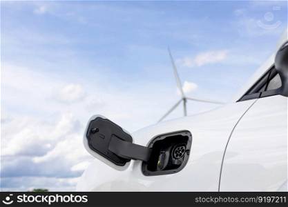 Progressive combination of wind turbine and EV car, future energy infrastructure. Electric vehicle being charged at charging station powered by renewable energy from wind turbine in the countryside.. Progressive combination of EV car, charging station and wind turbine.