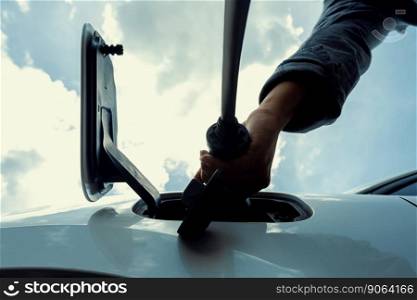 Progressive concept of electric rechargeable car, hand inserting charger device from electric charging station to EV car socket from below view with sky cloudscape background.. Progressive below view image of hand insert EV charger to socket with cloudscape