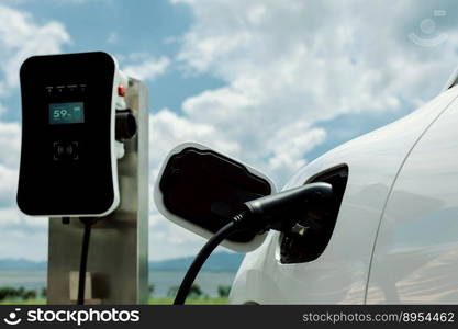 Progressive concept of electric vehicle, EV car alongside with charging station. Natural background of green field for clean environment for eco-car with renewable energy concept.. Progressive concept of EV car with charging point at natural green field scenery