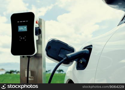 Progressive concept of electric vehicle, EV car alongside with charging station. Natural background of green field for clean environment for eco-car with renewable energy concept.. Progressive concept of EV car with charging point at natural green field scenery