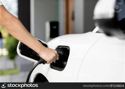 Progressive concept of hand insert an emission-free power connector to the battery of electric vehicle at home. Electric vehicle charging via cable from charging station to EV car battery. Progressive idea of charging electric vehicle via cable from charging station.