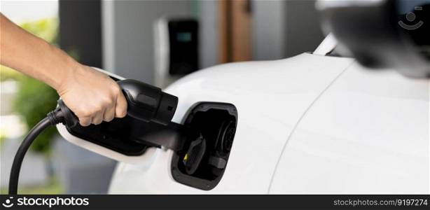 Progressive concept of hand insert an emission-free power connector to the battery of electric vehicle at home. Electric vehicle charging via cable from charging station to EV car battery. Progressive idea of charging electric vehicle via cable from charging station.