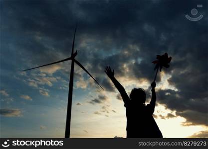Progressive concept of silhouette young asian boy playing with wind turbine toy in the wind turbine farm, green field over the hill. Green energy from renewable electric wind generator.. Progressive concept of silhouette young asian boy playing with wind turbine toy.