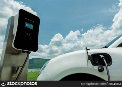 Progressive environmental green technology concept. Electric vehicle recharging battery at charging station powered by sustainable clean energy in natural green meadow with lakes and hills background.. Progressive concept of EV car with green field, hill and lake as background.