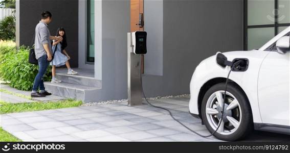 Progressive father and daughter plugs EV charger from home charging station to electric vehicle. Future eco-friendly car with EV cars powered by renewable source of clean energy.. Progressive dad and daughter charging EV car from home charging station.
