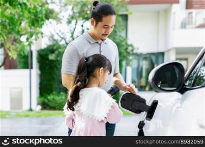Progressive father and daughter returned from school in electric vehicle that is being charged at home. Electric vehicle driven by renewable clean energy. Home charging station concept for environment. Progressive concept of father and daughter with EV car and home charging station