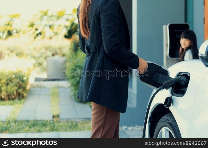 Progressive lifestyle of mother and daughter who have just returned from school in an electric vehicle that is being charged at home. Electric vehicle powered by sustainable clean energy.. Progressive lifestyle of mother and daughter with EV car and charging station.