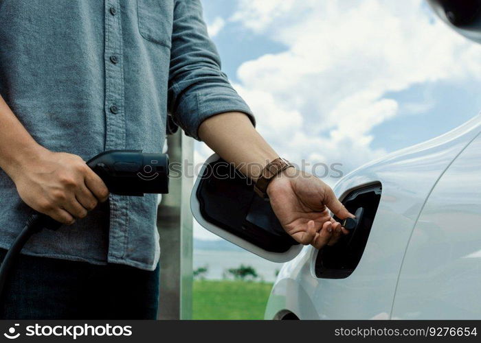 Progressive natural scenic where hand insert charging plug to electric vehicle from charging station with natural background. Future energy concept of EV car powered by sustainable electric energy.. Progressive natural scenic of hand insert charging plug to EV car.