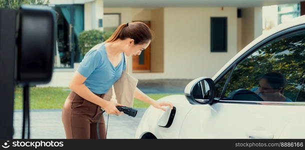 Progressive woman install cable plug to her electric car with home charging station. Concept of the use of electric vehicles in a progressive lifestyle contributes to clean environment.. Progressive woman recharge her EV car at home charging station.