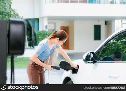 Progressive woman install cable plug to her electric car with home charging station. Concept of the use of electric vehicles in a progressive lifestyle contributes to clean environment.. Progressive woman recharge her EV car at home charging station.